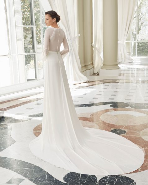 Boho-Brautkleid aus Georgette und Spitze. Rundhalsausschnitt, geschlossener Rücken und lange Raglanärmel. Vorne gefältelter Rock mit Schlitz. Mit Posamenten-Verzierungen an Oberteil und Ärmeln. Erhältlich in Naturweiß. Kollektion ROSA CLARA COUTURE 2019.