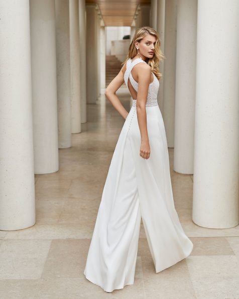 Leichtes Braut-Hosenkleid aus strassbesetzter Spitze und Crêpe. Hoher Rundhalsausschnitt und am Rücken gekreuzte Träger. Mit Eingrifftaschen, Knöpfen an den Schultern und Guipure-Verzierung am Gürtel. Kollektion ROSA CLARA COUTURE 2020.