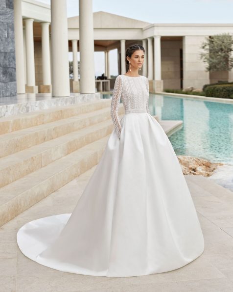 Classic tailored wedding dress in beaded lace and royal satin. With bateau neckline, V-back and long sleeves. Skirt with pleats at the waist and pockets. 2020 ROSA CLARA COUTURE Collection.
