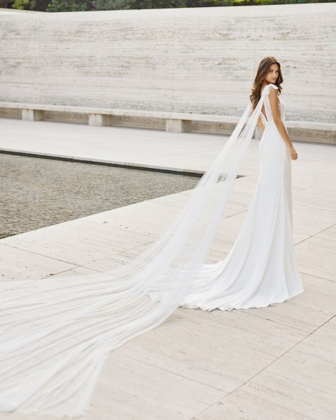 Vestido elegante de noiva, de corte reto com quedas removíveis de tule; com decote deep-plunge e costas em V de renda e peças brilhantes no decote e na cintura. Modelo de tendência da Rosa Clará feito com crepe elástico e renda, com detalhes de peças brilhantes, com forro modelador. Coleção ROSA CLARA 2022.